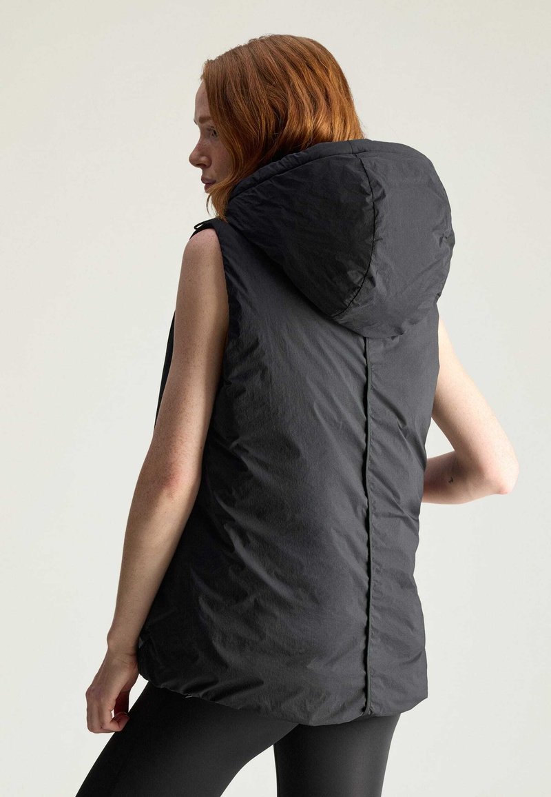 Mouwloze zwarte puffer vest met een capuchon, voorzien van een gladde textuur en een verticale naad in het midden, ontworpen voor warmte en comfort.