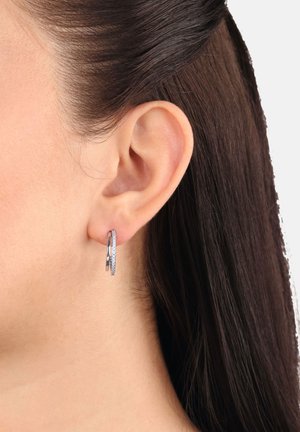 Primo piano di un orecchio femminile con capelli scuri e lisci, che indossa un orecchino a cerchio in argento adornato con piccole pietre trasparenti.