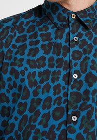 Korte mouwen overhemd in een blauwe stof met een zwart en groene luipaardprint. Inclusief een kraag en zilveren knopen. Geverfde uitstraling.