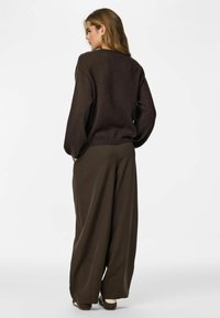 Maglione marrone lavorato a maglia con maniche a palloncino, abbinato a pantaloni scuri a gamba larga. Tessuto liscio, vestibilità rilassata e dettagli di design sottili.