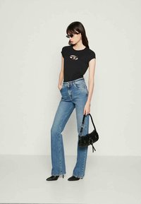 Black fitted t-shirt with cutout detail, light blue flared jeans, black heeled boots, and a small black handbag with silver accents.