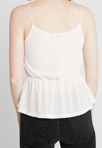 Top peplum bianco con spalline regolabili, tessuto leggero, vita arricciata e una finitura morbida e texturizzata.