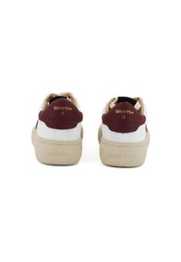 Sneakers bianchi con accenti bordeaux e branding dorato sul tallone. Design arrotondato con suola testurizzata e intersuola color crema.