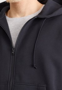 Mörkblå zip-up hoodie gjord av mjukt tyg, med dragsko i huva, framfickor och slät dragkedjestängning.