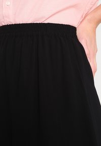 Gonna nera con fascia elasticizzata, caratterizzata da un design fluido e una texture liscia. Mano visibile in tasca, che enfatizza i dettagli pratici.