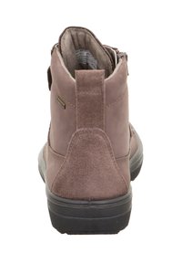 Stivaletti alla caviglia in suede marrone con collo imbottito, suola in gomma e linguetta sul retro. Presentano una texture liscia e un design minimalista.