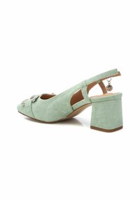 Tacón slingback de ante verde menta con un tacón bloque, lazo decorativo y detalle de strass en la punta, y una correa en el tobillo para mayor soporte.