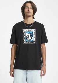 Sort bomulds t-shirt med et grafisk design i blå og hvid, med en rektangulær ramme og logo i midten. Korte ærmer, afslappet pasform.