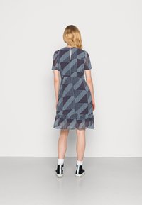 Vestuário de manga curta, ao comprimento do joelho, em azul-marinho com um padrão geométrico de bolinhas, apresentando uma bainha com frufru e uma abertura em forma de olho-chave nas costas. Complementado por botas pretas.