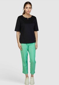 Black short-sleeve top with a keyhole neckline, paired with green cropped pants featuring side zippers and white sneakers.