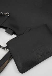 Sac à main en cuir noir texturé avec pochette détachable et quincaillerie argentée sur une surface claire.