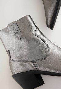 Bottes de cheville métalliques argentées avec une texture craquelée, des coutures noires et un petit talon rectangulaire. Design supérieur sans couture avec un accent de tirette.