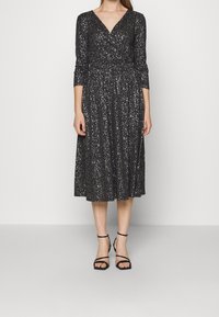 Robe noire de longueur genou avec un décolleté en V, des manches trois-quarts et des détails en paillettes argentées. Assortie à des chaussures à talons striées noires.