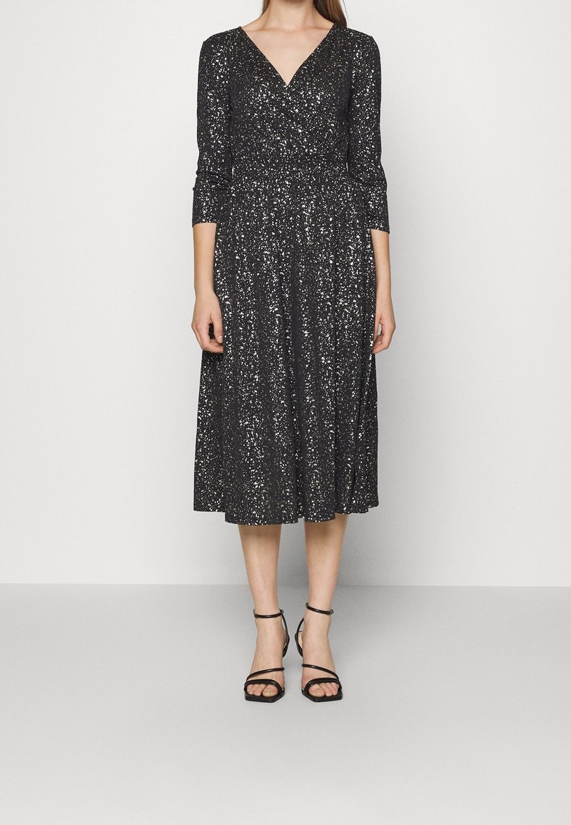 Robe noire de longueur genou avec un décolleté en V, des manches trois-quarts et des détails en paillettes argentées. Assortie à des chaussures à talons striées noires.