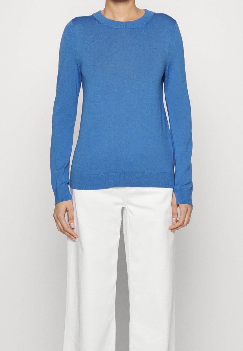 Pull bleu à manches longues en matière tricotée avec un col rond. Associé à un pantalon blanc à jambes larges. Présente une texture lisse.