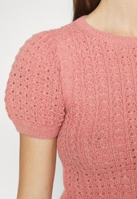 Top de punto en suave color rosa con mangas cortas abullonadas. Presenta un patrón texturizado de puntos abiertos y puños acanalados, proporcionando una silueta ajustada.