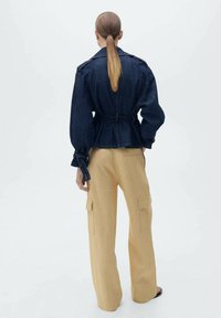 Denimjas met puffy mouwen, een getailleerde taille en strikaccenten; gecombineerd met beige cargobroek met wijde pijpen en zijzakken.