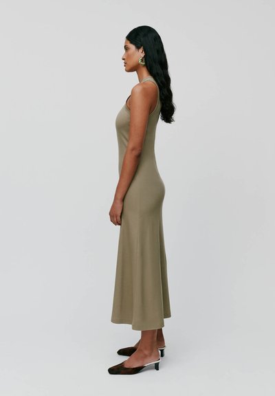 Abito maxi senza maniche di colore verde oliva con corpetto aderente e gonna fluida, realizzato in materiale elastico. La modella indossa mule nere.