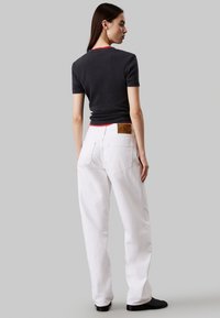 T-shirt nera a coste aderente con maniche corte e collo rosso, abbinata a jeans bianchi larghi in denim con tasche posteriori e un'etichetta marrone.