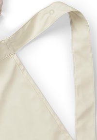 Ljusbeige axelväska med en slät yta och justerbar rem, med stickningar upptill och en tryckknappdetalj.