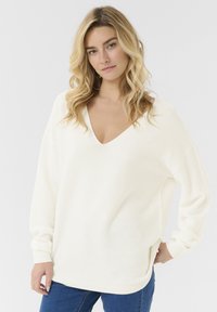 Cremefarbenes, oversized V-Ausschnitt-Pullover mit langen Ärmeln und gerippter Textur. Verfügt über einen lässigen Schnitt und seitliche Schlitze für mehr Bewegungsfreiheit.