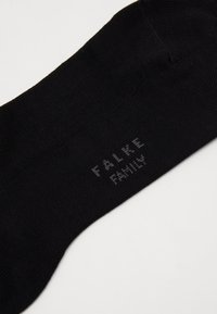 Calcetín negro con textura acanalada. Presenta el logotipo en gris claro "FALKE FAMILY" tejido cerca del puño. Diseño clásico sin patrones ni acentos adicionales.