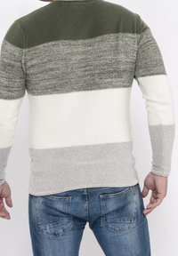 Langärmliger Pullover mit Farbblock-Design: dunkelgrün, grau, weiß und hellgrau. Stricktextur, Rundhalsausschnitt, taillierte Silhouette. Denim-Jeans sind sichtbar.