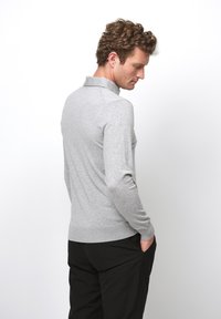 Grå långärmad polo tröja med krage, som har en figursydd design och ribbade cuffs. Matchad med svarta byxor. Bakvy.