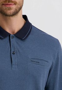 Herren Poloshirt in Marineblau mit strukturiertem Muster, kontrastierendem Kragen und einer Brusttasche mit Logodetail. Mit Knöpfen an der Vorderseite.