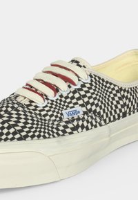 Παπούτσι Vans χαμηλού τύπου με ασπρόμαυρο καρό σχέδιο, λευκά κορδόνια και μπεζ σόλα και εσωτερική επένδυση.