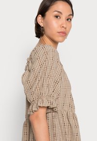 Vestido padrão bege com um corte descontraído, featuring mangas curtas bufantes, acentos com babados e uma silhueta em camadas com um discreto design em grelha.