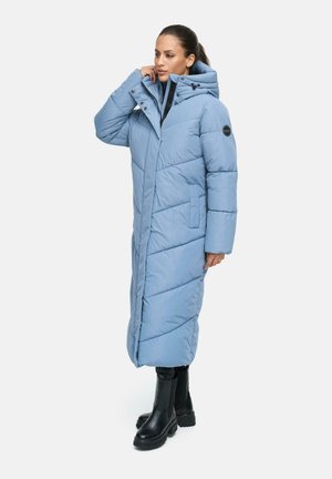 Lange lichtblauwe gewatteerde jas met een hoge kraag, diagonale quiltstiksels, zijzakken en knoopsluitingen, gestyled met zwarte enkellaarzen.