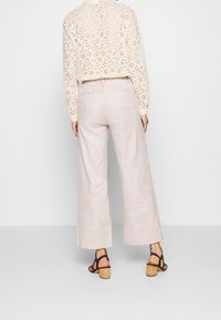 Svetle béžové široké lněné kalhoty s hladkou texturou, spárované s krémovým krajkovým topem s květinovým vzorem a otevřeným zadním dílem.