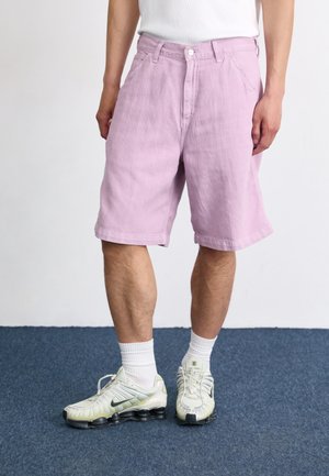 Lavender Baumwollshorts mit lockerer Passform, ausgestattet mit einem Reißverschluss, seitlichen Taschen und einem gesäumten Rand, kombiniert mit weißen Sportsocken und Sneakers.