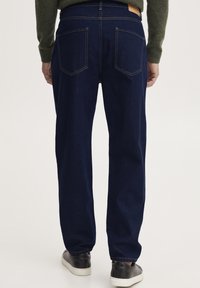 Temno modri jeans hlače s sproščenim krojem, ki imajo dve zadnji žep, kontrastno šivanje in usnjeno oznako na pasu.