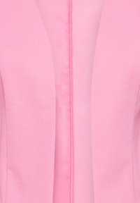 Pietuvināts rozā bleizera žaketes skats, rādot priekšējos atlokus un centrālo šuvi ar gludu auduma tekstūru.