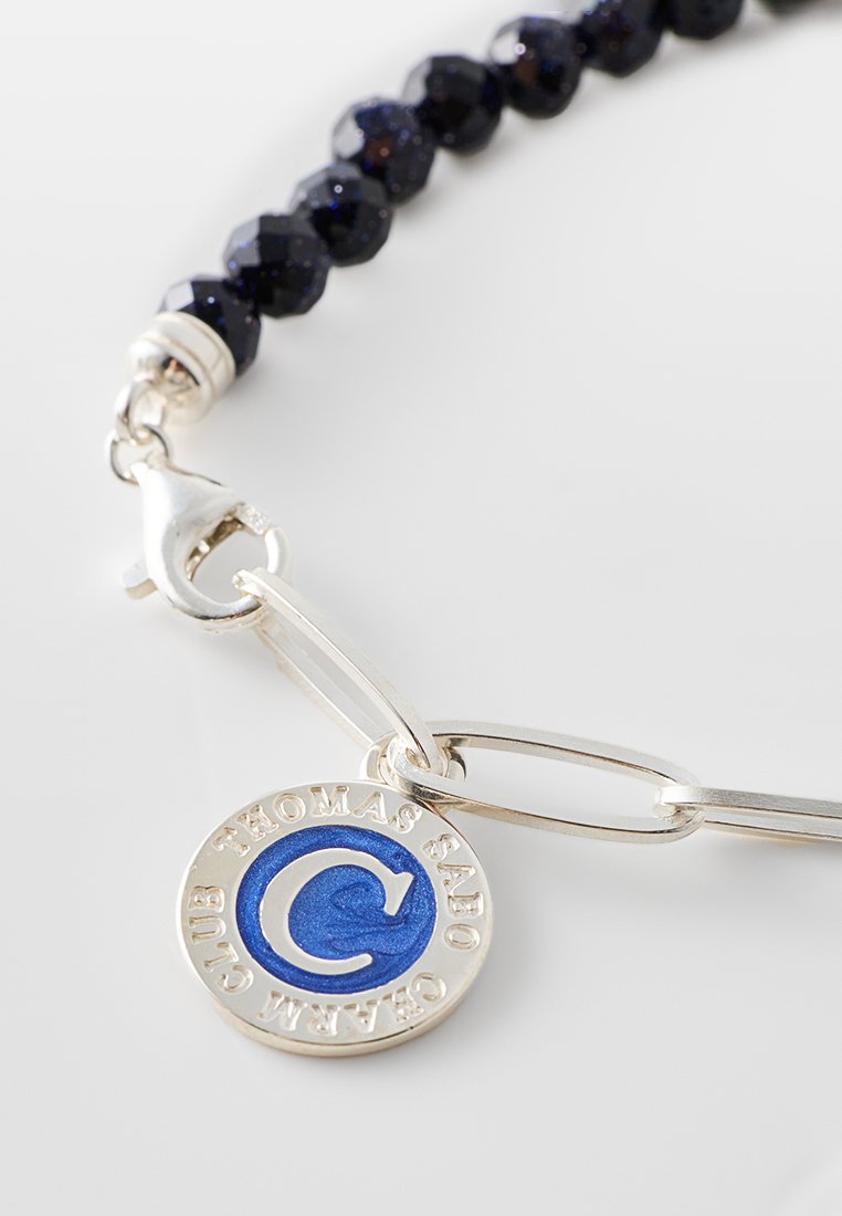 Perlenarmband aus dunklen blauen facettierten Glasperlen, mit einem silbernen Verschluss und einem runden silbernen Anhänger mit einem blauen Emblem.