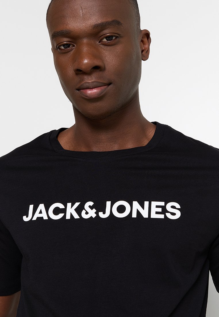 Camiseta negra de algodón con cuello redondo. Presenta un texto en blanco llamativo "JACK & JONES" en el pecho. Diseño simple y casual.