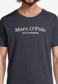 T-shirt in cotone blu navy con collo rotondo e maniche corte, con la scritta "Marc O'Polo EST. IN STOCKHOLM" stampata in bianco.