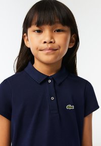 Navyblauwe polo met korte mouwen, gestructureerde stof, geribde kraag en een groene krokodillenlogo op de linkerborst.