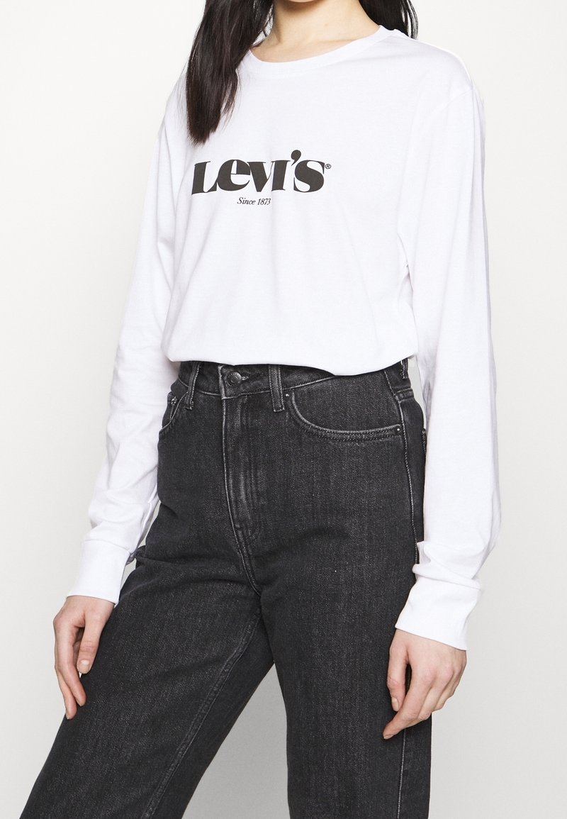 Weißes Langarm-T-Shirt mit schwarzem "Levi's"-Logo, kombiniert mit hochtaillierten dunkelblauen Jeans aus Denim mit klassischem Fünf-Taschen-Design.