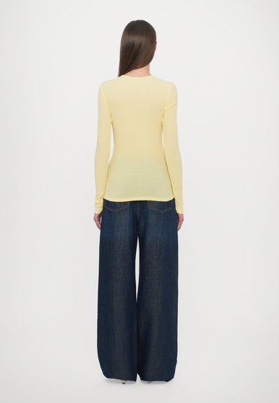 Yellow long-sleeve top with a fitted silhouette paired with wide-leg dark blue denim pants, featuring back pockets and a smooth texture.
