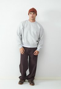 Szary sweter z prążkowanym dołem, w połączeniu z ciemnobrązowymi spodniami o szerokich nogawkach. Brązowa dziana beanie i brązowe buty z dekoracyjnym przeszyciem.