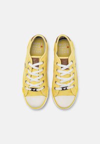Yellow canvas sneakers with white laces and rubber toe caps. Feature textured insole with "MUSTANG TRUE DENIM" branding in gray.
