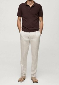 Brązowa koszulka polo, jasnobeżowe spodnie i brązowe sandały. Spodnie mają elastyczną talię i sznurek do wiązania.