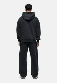 Zwarte oversized hoodie met een capuchon en bijpassende wijde broek. De stof lijkt zacht, met een gestructureerde afwerking en een casual silhouet.