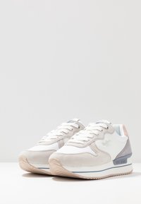 Sneaker bianco e grigio con materiali in suede e mesh, punta rotonda, suola testurizzata, dettagli rosa sul tallone e logo del brand sul lato.