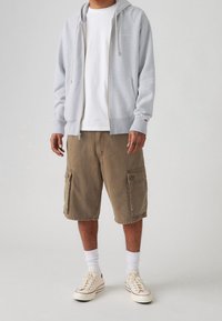 Gray zip-up hoodie, white t-shirt, brown cargo shorts, white socks, and beige sneakers. Features include drawstrings and side pockets.
