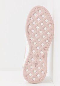 Semelle d'une basket rose clair avec motif diamant et coussinet blanc visible en dessous, arborant la marque "MICHAEL KORS" au centre.