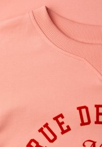 Różowa bluza z prążkowanym, okrągłym dekoltem i czerwonym napisem „RUE DE”, wykonana z gładkiej, miękkiej tkaniny.